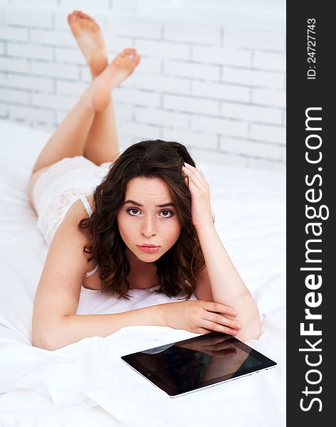 Beautiful emotional young woman using tablet computer in her bedroom high key. Beautiful emotional young woman using tablet computer in her bedroom high key