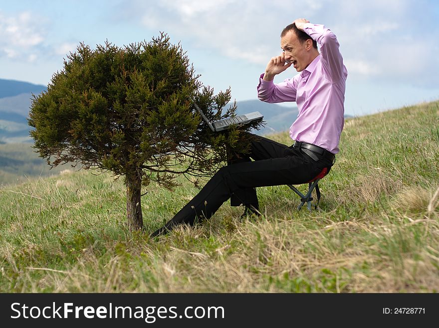 Man works on computer, located on tree and speaks on telephone. Man works on computer, located on tree and speaks on telephone