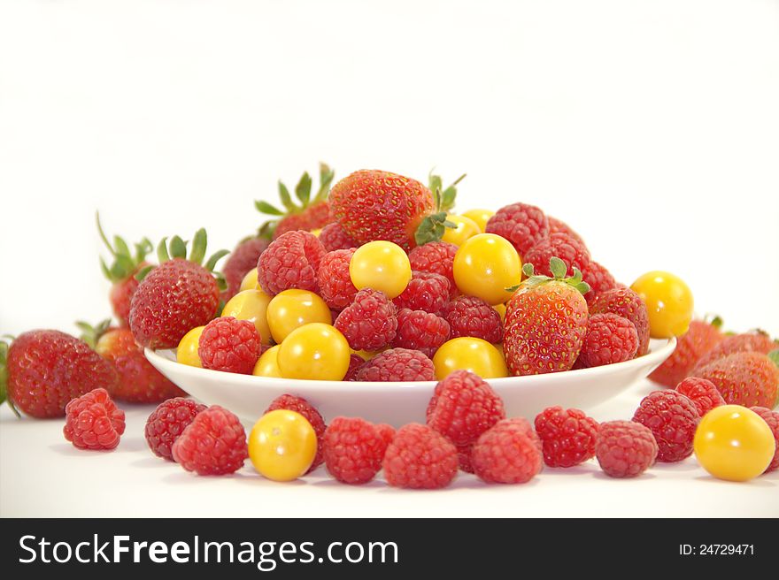 Fresh raspberries, strawberries and gooseberries on the plate on white background