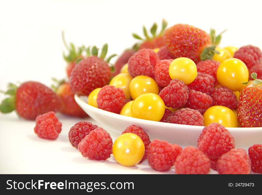 Raspberries, gooseberries and strawberries on the plate on white background