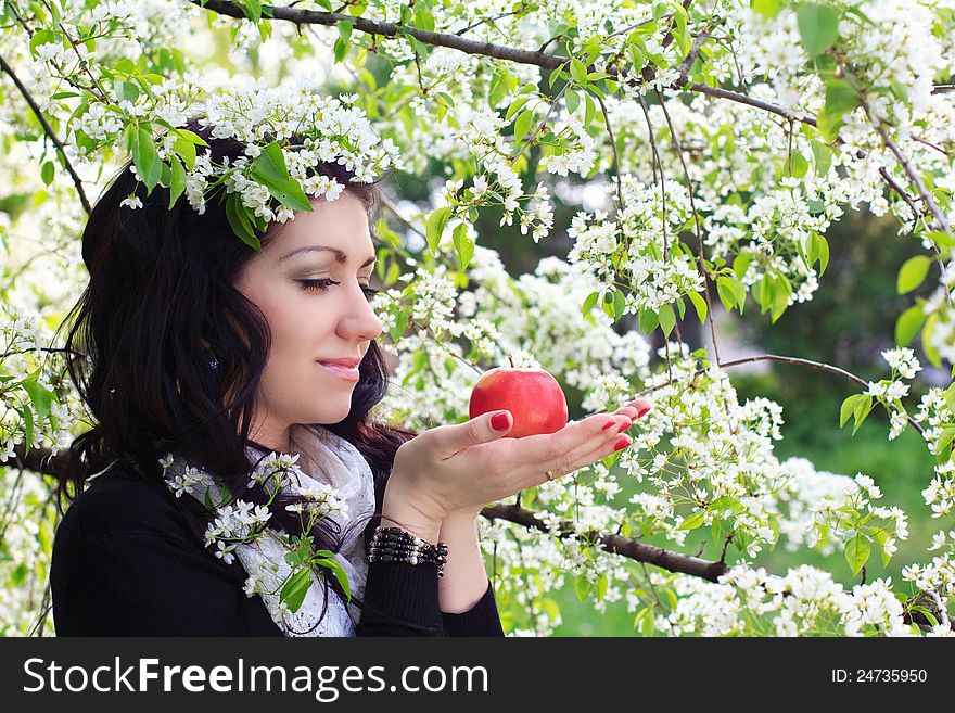 Young woman holding apple against the backdrop of flowering trees