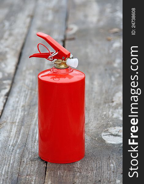 The compact fire extinguisher, which stands on an old wooden sidewalk. The compact fire extinguisher, which stands on an old wooden sidewalk