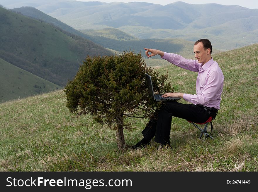 Man works on computer, located on tree. shows index fingers on sky. Man works on computer, located on tree. shows index fingers on sky.