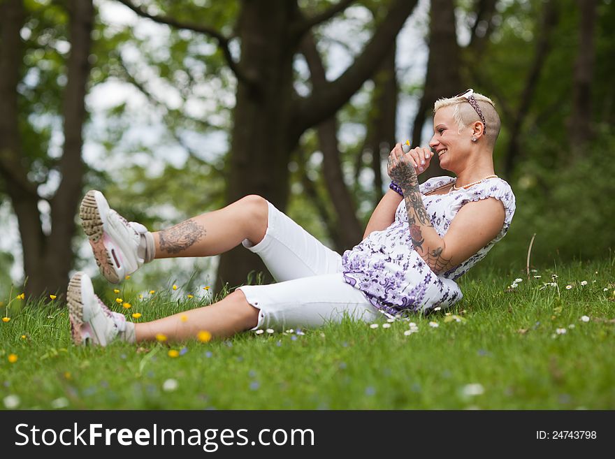 Beautiful tattooed woman sits in the grass and laughs. Beautiful tattooed woman sits in the grass and laughs