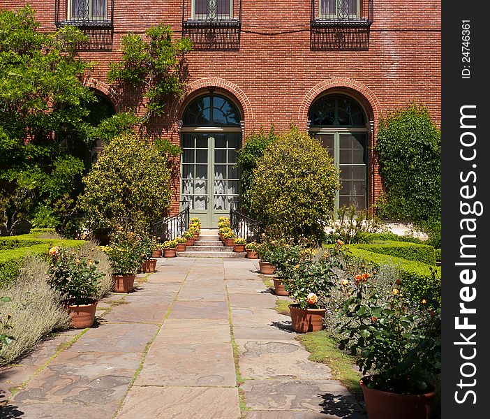 Red brick building with French door opening toward the garden. Beautiful flowers in pots on each side of the stairs. Red brick building with French door opening toward the garden. Beautiful flowers in pots on each side of the stairs