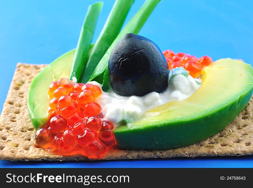 Crackers with cheese, sliced ​​avocado, green onion, red caviar and black olive. Crackers with cheese, sliced ​​avocado, green onion, red caviar and black olive