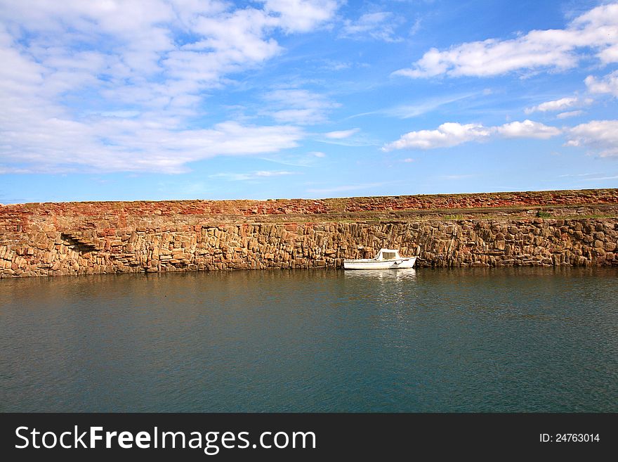 Old, fishing harbour in Dunbar with stone wall and a small white boat. Old, fishing harbour in Dunbar with stone wall and a small white boat