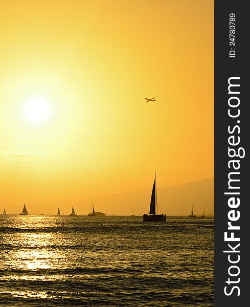 Sailboats and airplane over Hawaiian sunset