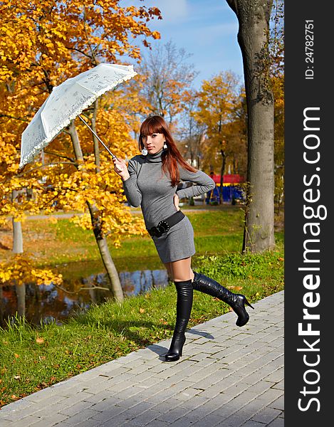 Young beautiful redhead girl with an umbrella in a city park in autumn. Young beautiful redhead girl with an umbrella in a city park in autumn