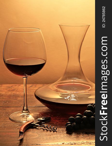 Red elegant wine glass and filled decanter. On wood with warm backlight. Red elegant wine glass and filled decanter. On wood with warm backlight