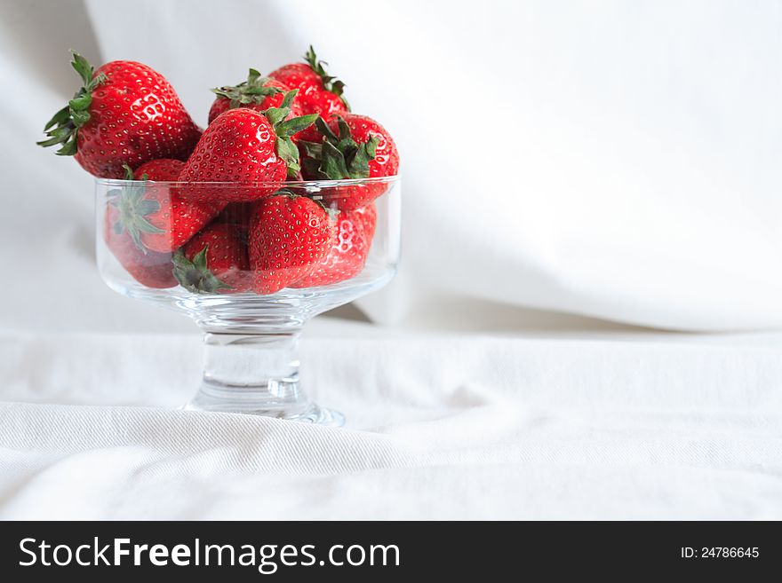 Transparent glass vase full of red strawberries on white textile background with free space for text. Transparent glass vase full of red strawberries on white textile background with free space for text