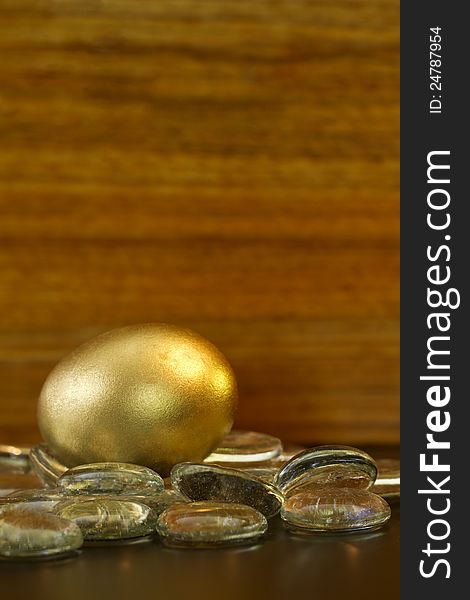 Gold egg glistens on glass stones in front of wood grain background; vertical image with copy space at top;. Gold egg glistens on glass stones in front of wood grain background; vertical image with copy space at top;