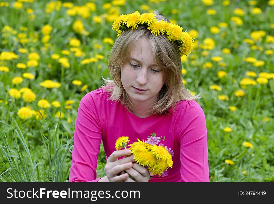 Happy girl in a wreath from yellow dandelions admires flowers. Happy girl in a wreath from yellow dandelions admires flowers