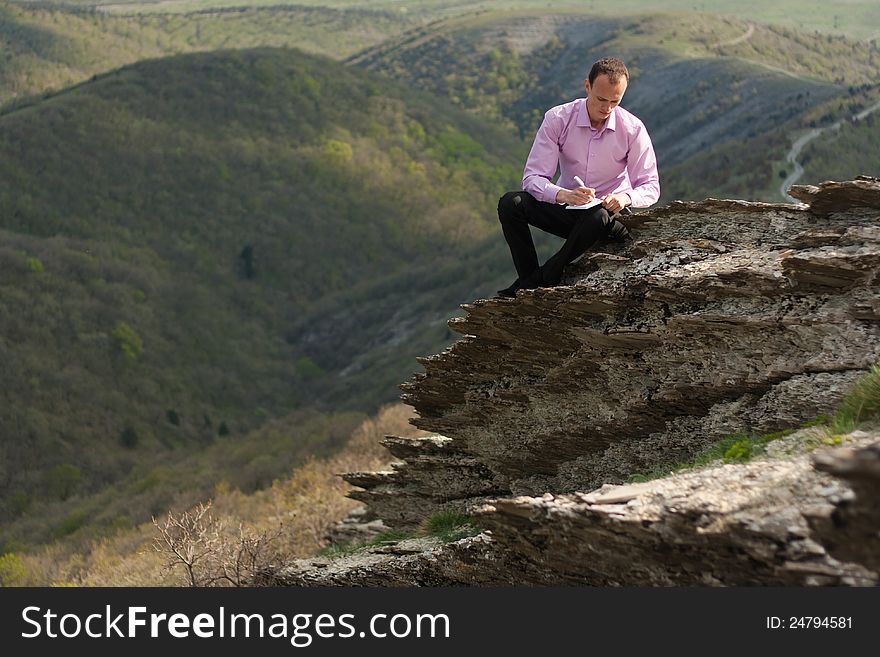 Man writes in notepad sitting on stone. Man writes in notepad sitting on stone