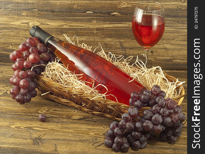 Bottle of pink wine in a basket and fresh grapes on a table. Bottle of pink wine in a basket and fresh grapes on a table.