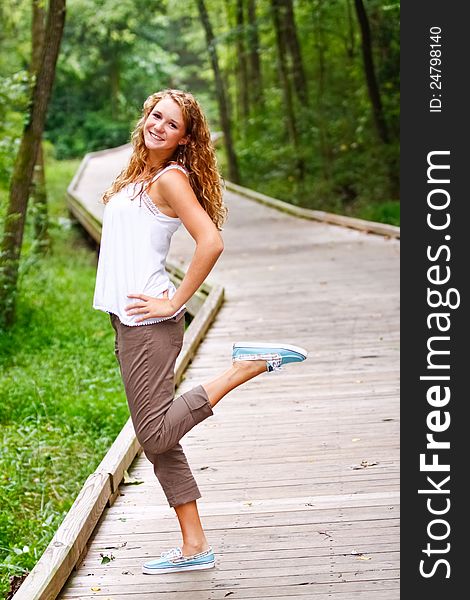 A beautiful blond teenage girl next door with curly hair wearing a white top having fun outdoors on a boardwalk in a local park. A beautiful blond teenage girl next door with curly hair wearing a white top having fun outdoors on a boardwalk in a local park.