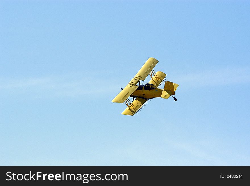 A yellow biplane crop duster preparing to make a pass over a field.