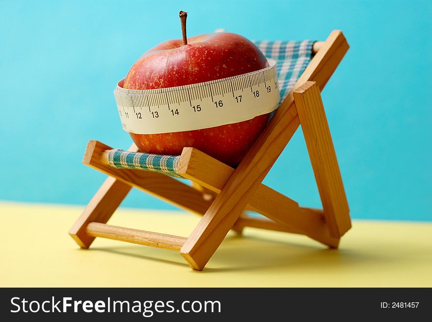 Healthy holidays, conceptual photo. An apple on a deckchair and measuring tape. Healthy holidays, conceptual photo. An apple on a deckchair and measuring tape.