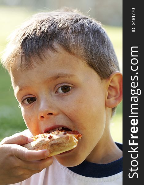 Cute young boy eating pizza outside