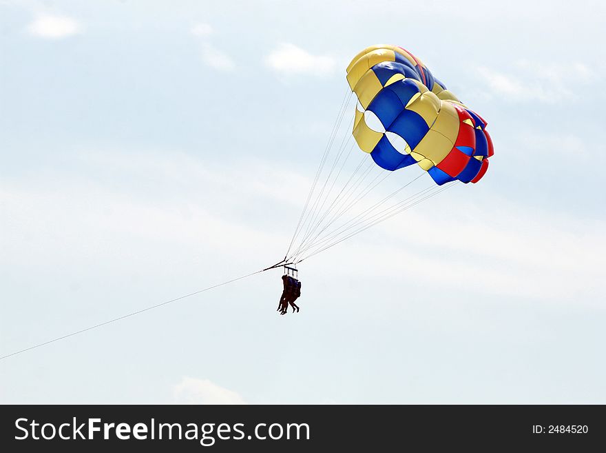 Three people parasailing against a light blue sky