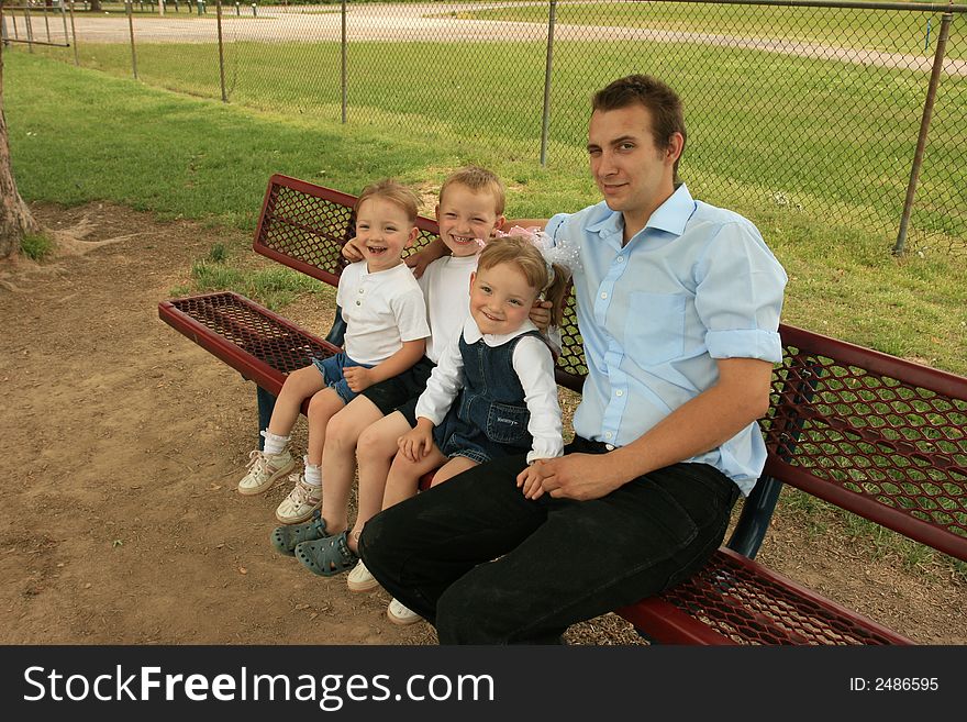 Father, son, and twin daughters sitting on a bench at the playground. Father, son, and twin daughters sitting on a bench at the playground