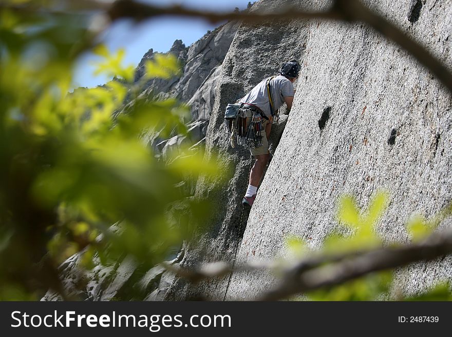 A man  on a rock climb view through the trees. A man  on a rock climb view through the trees