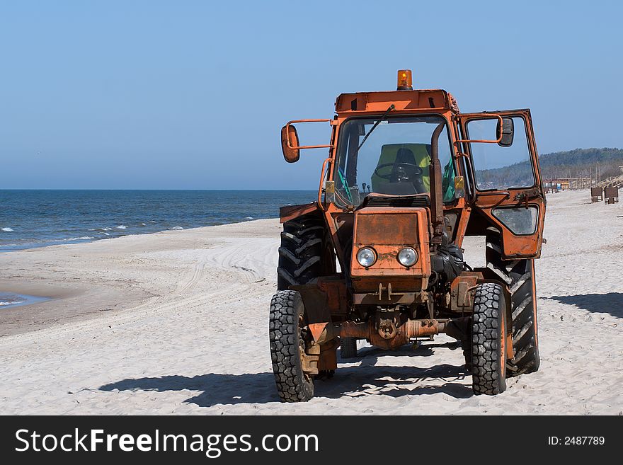 Old orange colored tractor on the deserted beach. Old orange colored tractor on the deserted beach
