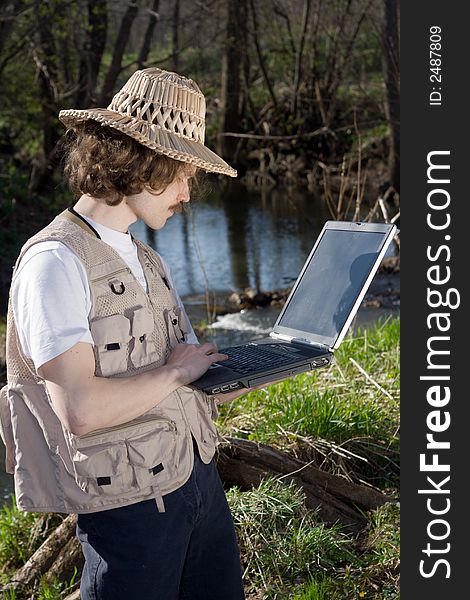 Man with portable computer standing and looking for something near small river at nature.