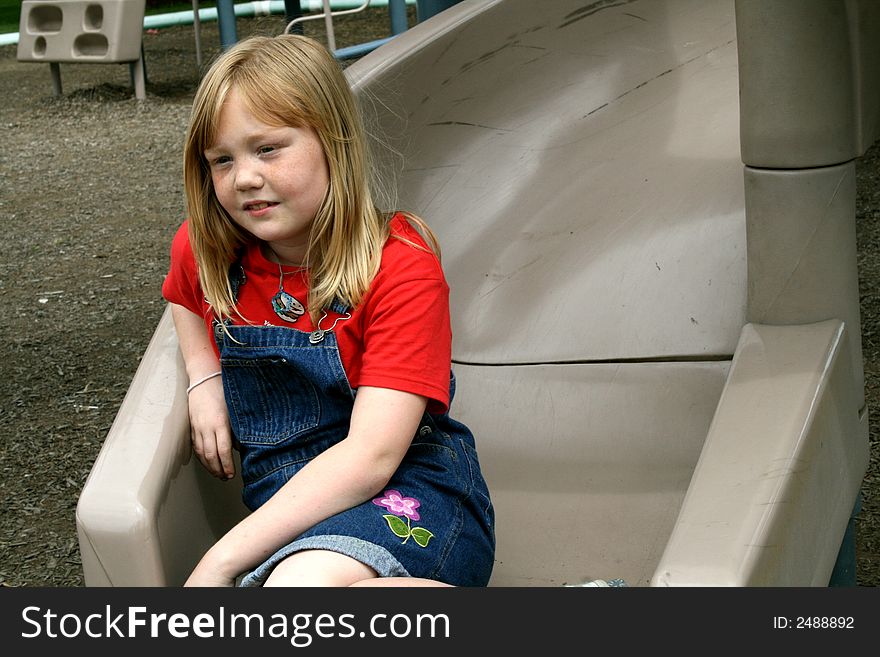 Young girl with red hair and freckles playing on the slide at the park. Young girl with red hair and freckles playing on the slide at the park