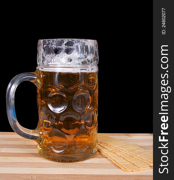 Glass of fresh beer with foam and chips on a black background