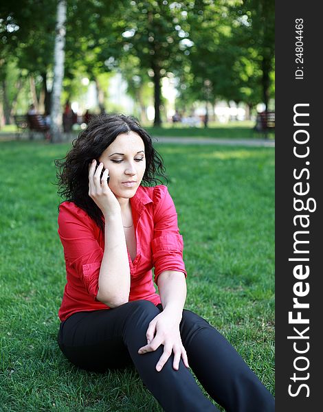 Girl with the phone sitting on the grass in the summer