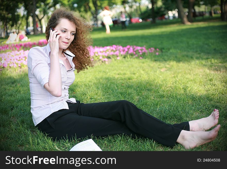 Curly-haired girl with the phone sitting on the grass in the summer