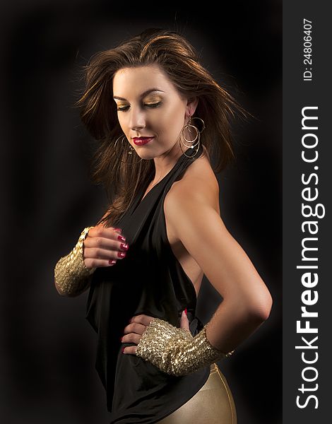 Beautiful woman with dramatic golden makeup, red lips, red nails, gold earrings and gloves looking down with her long hair blowing against black background. Beautiful woman with dramatic golden makeup, red lips, red nails, gold earrings and gloves looking down with her long hair blowing against black background