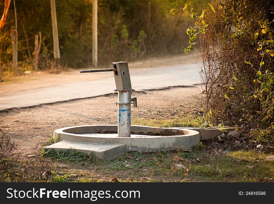 Old hand operated water pump standing on road side in the forest