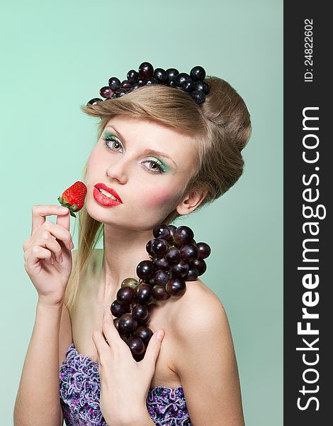 Young woman with strawberry and bunch of grapes, on green background