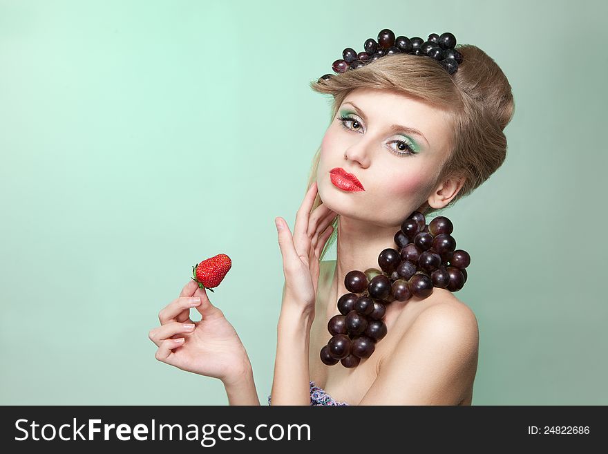 Young woman with strawberry and bunch of grapes, on green background with place for text