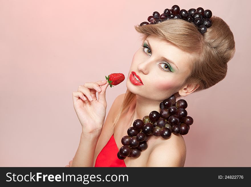 Young woman with strawberry and bunch of grapes, on pink background