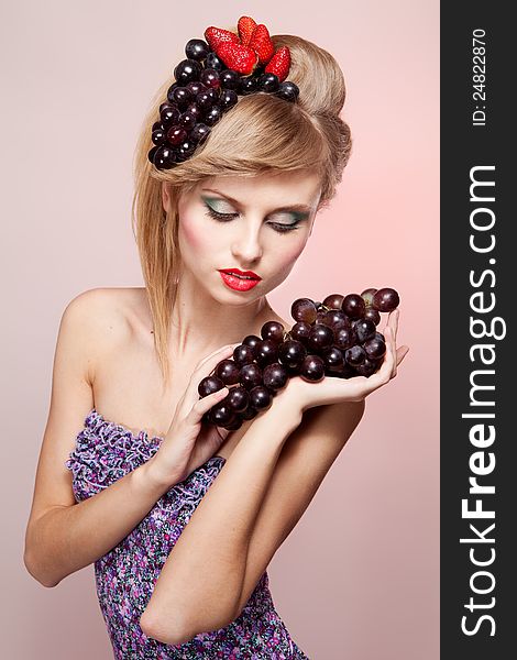 Young woman with strawberry and bunch of grapes in her hairs, on pink background