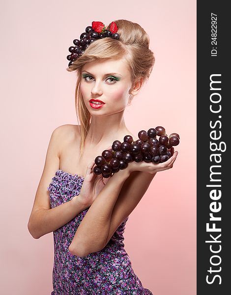 Young woman with strawberry and bunch of grapes looking at camera