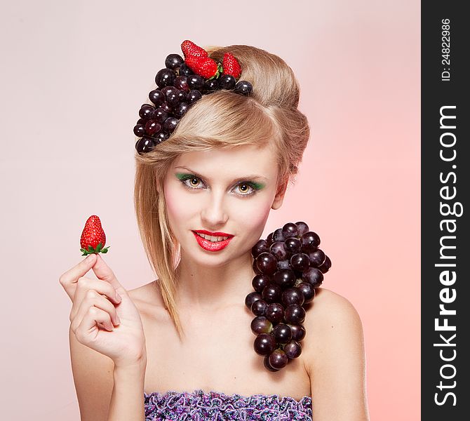 Young woman with strawberries and bunch of grapes holding a strawberry