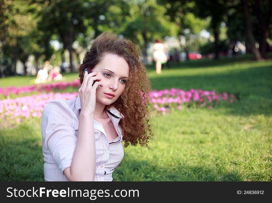 Cute curly girl talking on the phone in the park