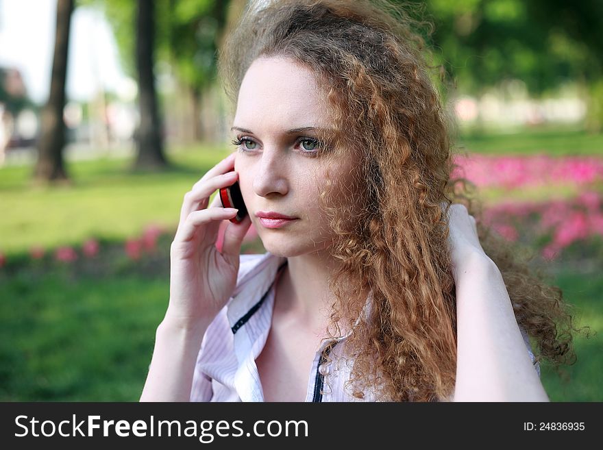 Portrait of a pretty girl with curly phone in park