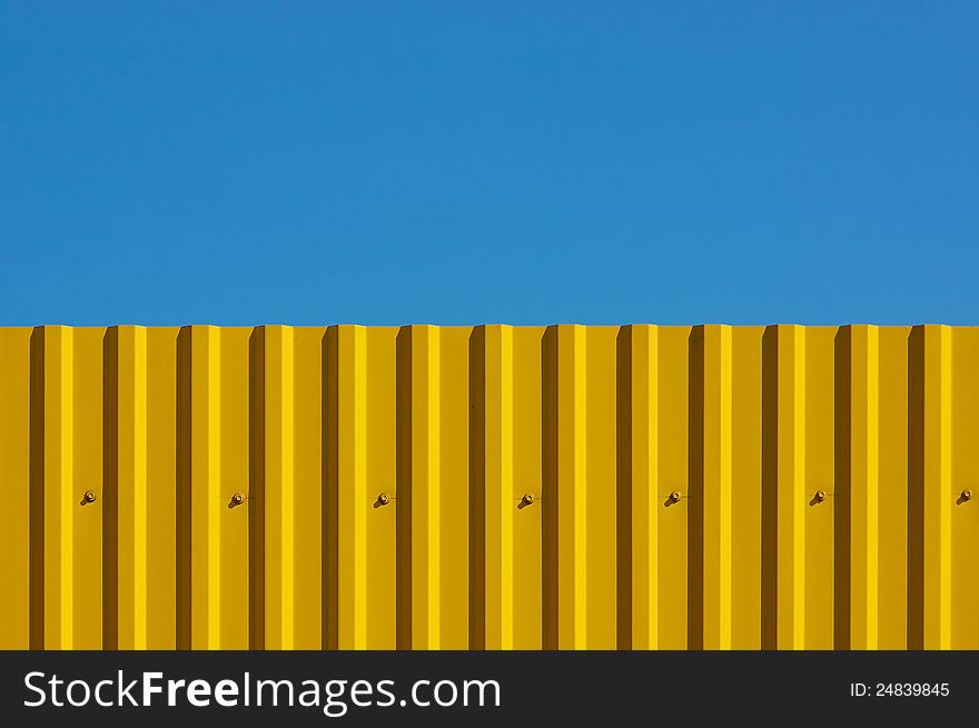 Fence made of corrugated yellow against the blue sky. It looks like a flag of Ukraine. Fence made of corrugated yellow against the blue sky. It looks like a flag of Ukraine