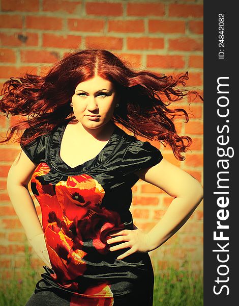 Beautiful young redhead woman with flying long hair on the background of a red brick wall. Beautiful young redhead woman with flying long hair on the background of a red brick wall