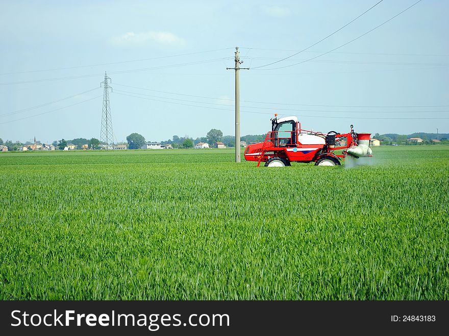 Red tractor waters a cultivated field in farmlands