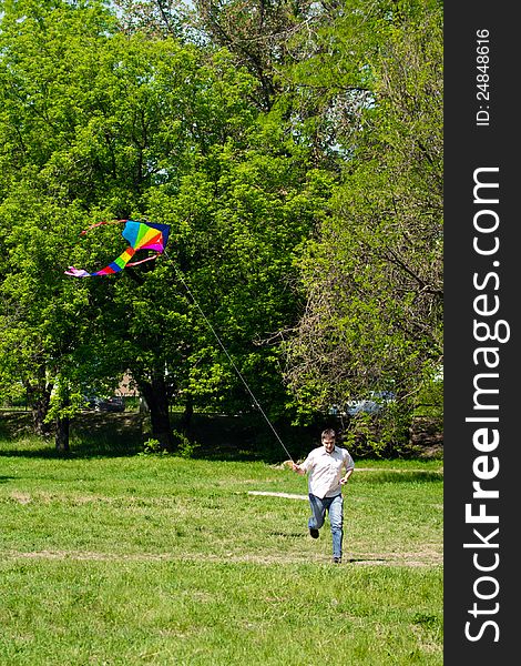 Man running over a green meadow in summer; he fly a kite. Man running over a green meadow in summer; he fly a kite