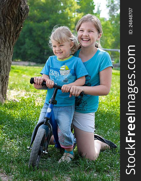 Two sisters sitting on a small bike and laughing. Two sisters sitting on a small bike and laughing