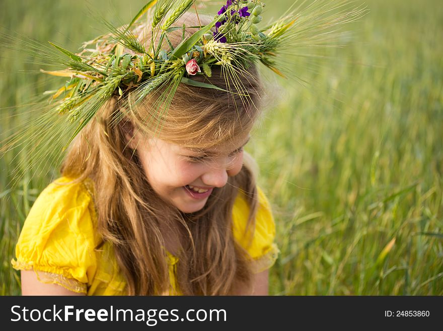 Beautiful little girl on the meadow. A wreath of wheat ears and wild flowers is on her blonde hair