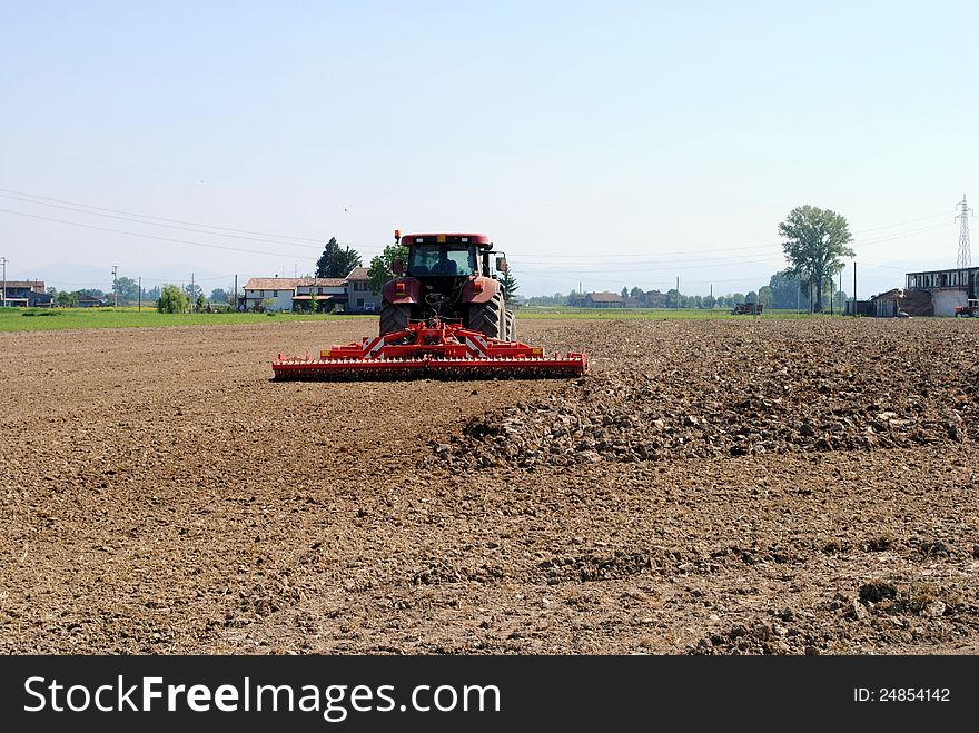 Red tractor prepares soil for seed in farmlands
