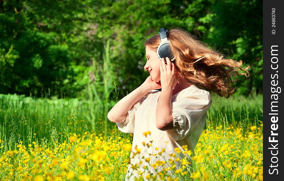 Beautiful girl in headphones enjoying the music with flowing hair in a field of flowers in nature. Beautiful girl in headphones enjoying the music with flowing hair in a field of flowers in nature